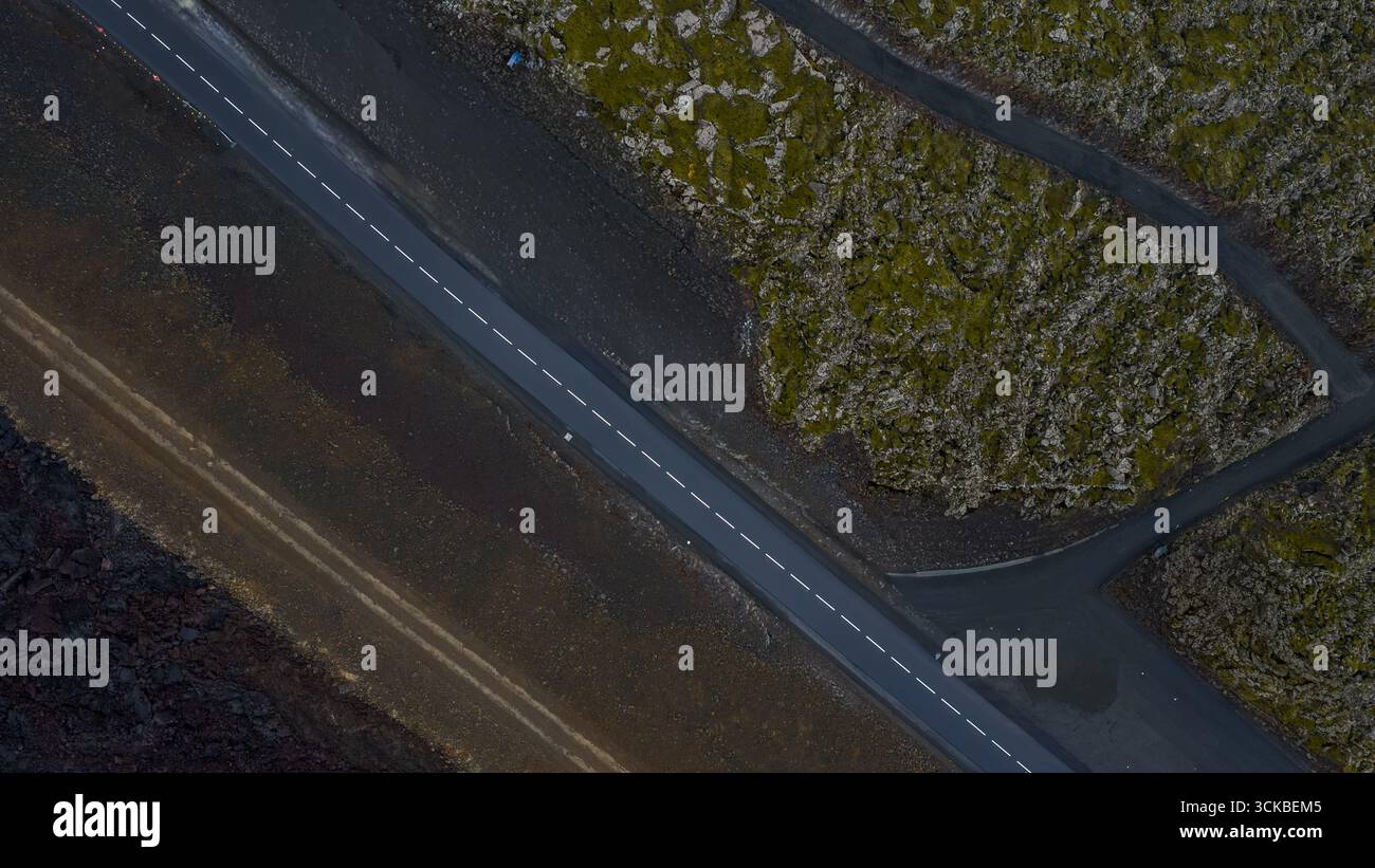 Una strada asfaltata dritta divide il terreno vulcanico coperto di muschio e il terreno arido in Islanda, mostrando texture contrastanti e paesaggi aspri. Foto Stock