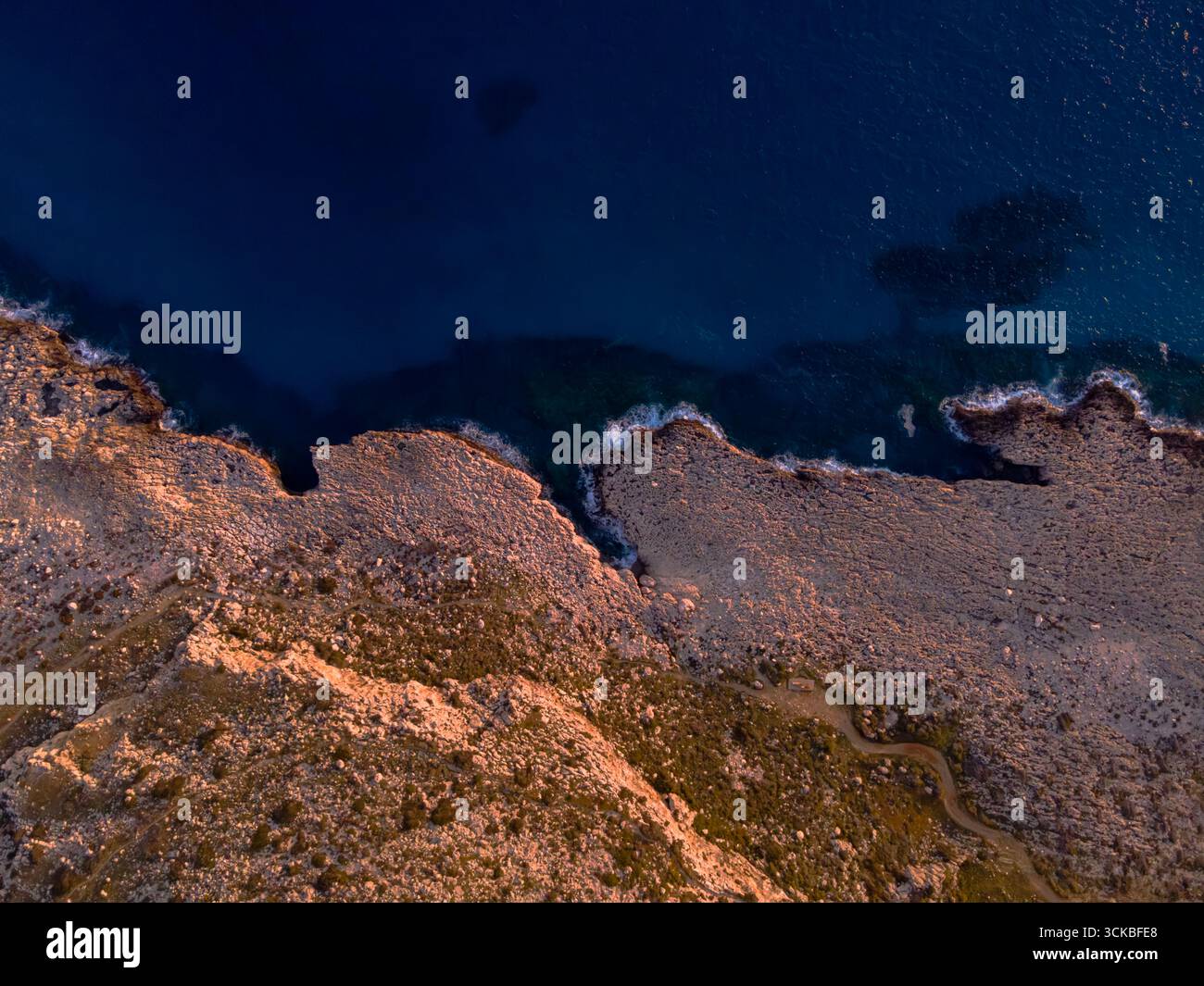 Vista aerea della costa di Cipro con scogliere rocciose, acque turchesi del Mediterraneo e un sentiero tortuoso lungo il terreno dorato durante il Golden hou Foto Stock