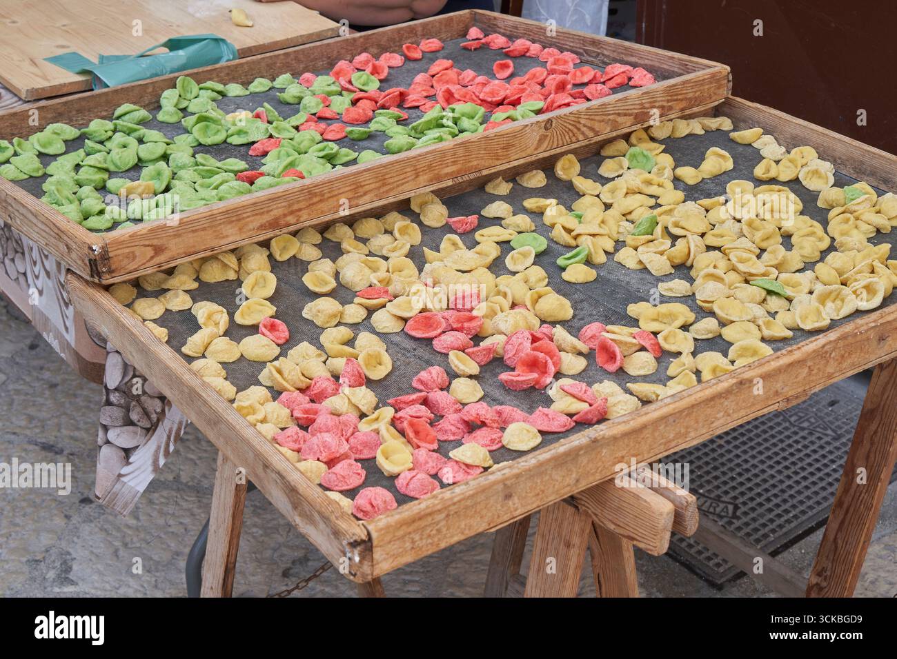 Pasta di orecchiette fatta a mano dai colori vivaci che si asciugano su piatti rustici in legno, tipica tradizione culinaria italiana. Foto Stock