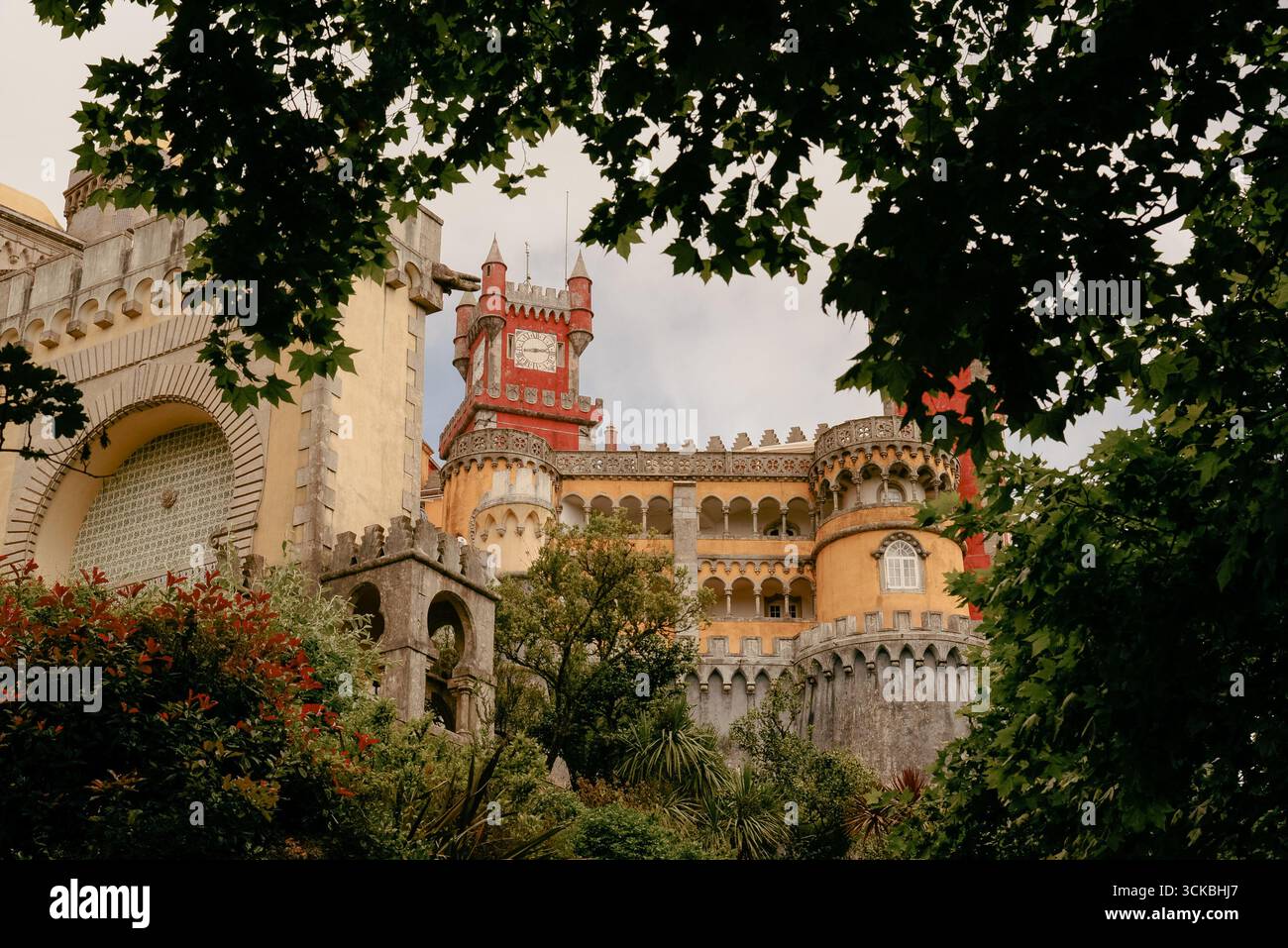 Vista esterna del Palácio da pena, un castello romanticista del XIX secolo situato a Sintra, Portogallo, incorniciato da rami di alberi. Foto Stock