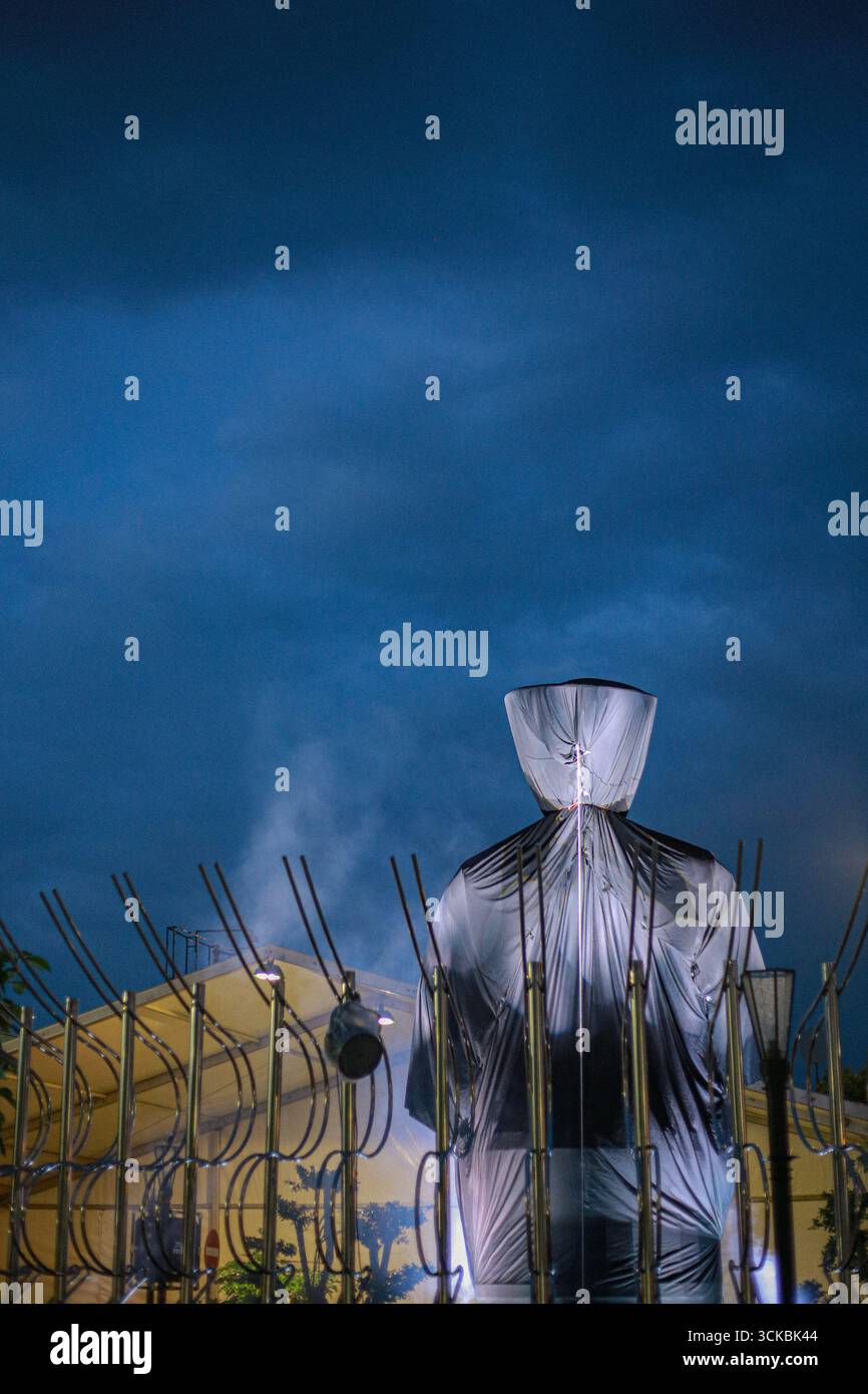 Una figura rivestita di plastica si staglia contro un cielo spettacolare, circondato da aste di metallo. La scena evoca un senso di mistero e intrigo. Foto Stock