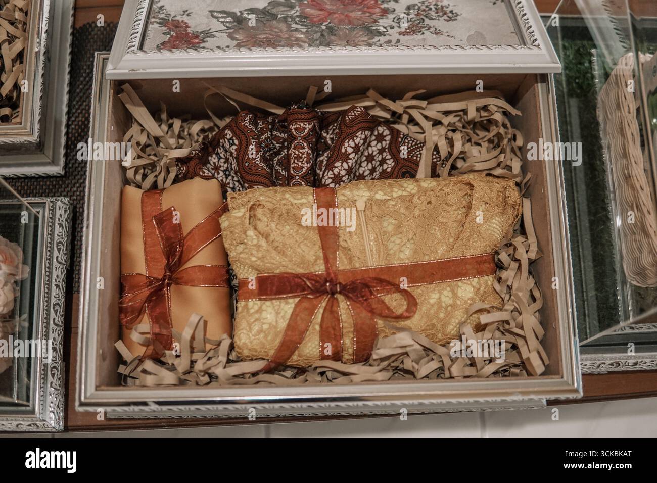 Una scatola regalo splendidamente disposta contenente articoli confezionati con nastri decorativi, circondata da uno stucco di carta straccia Foto Stock