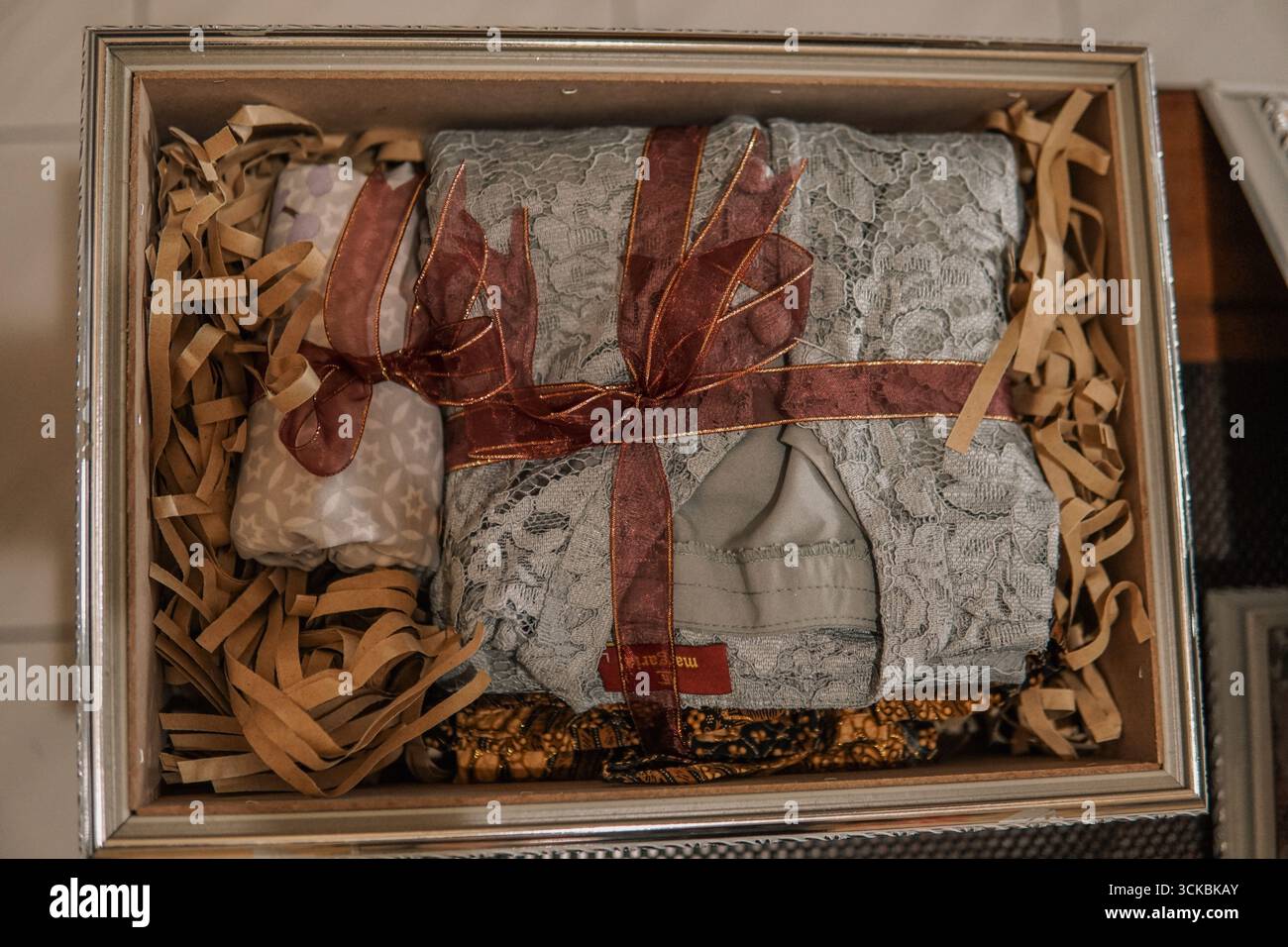 Una scatola regalo splendidamente confezionata contenente abiti in pizzo e oggetti decorativi, circondata da riempitivo di carta strappata Foto Stock