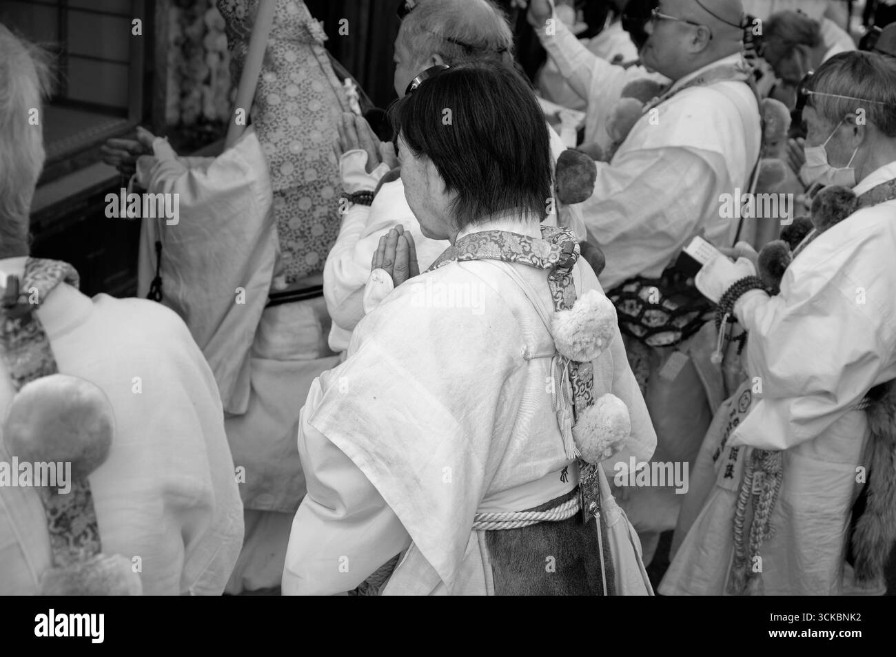 La donna anziana in abiti tradizionali si inchina in preghiera durante il Festival Tōka Ebisu di Kyoto in bianco e nero Foto Stock
