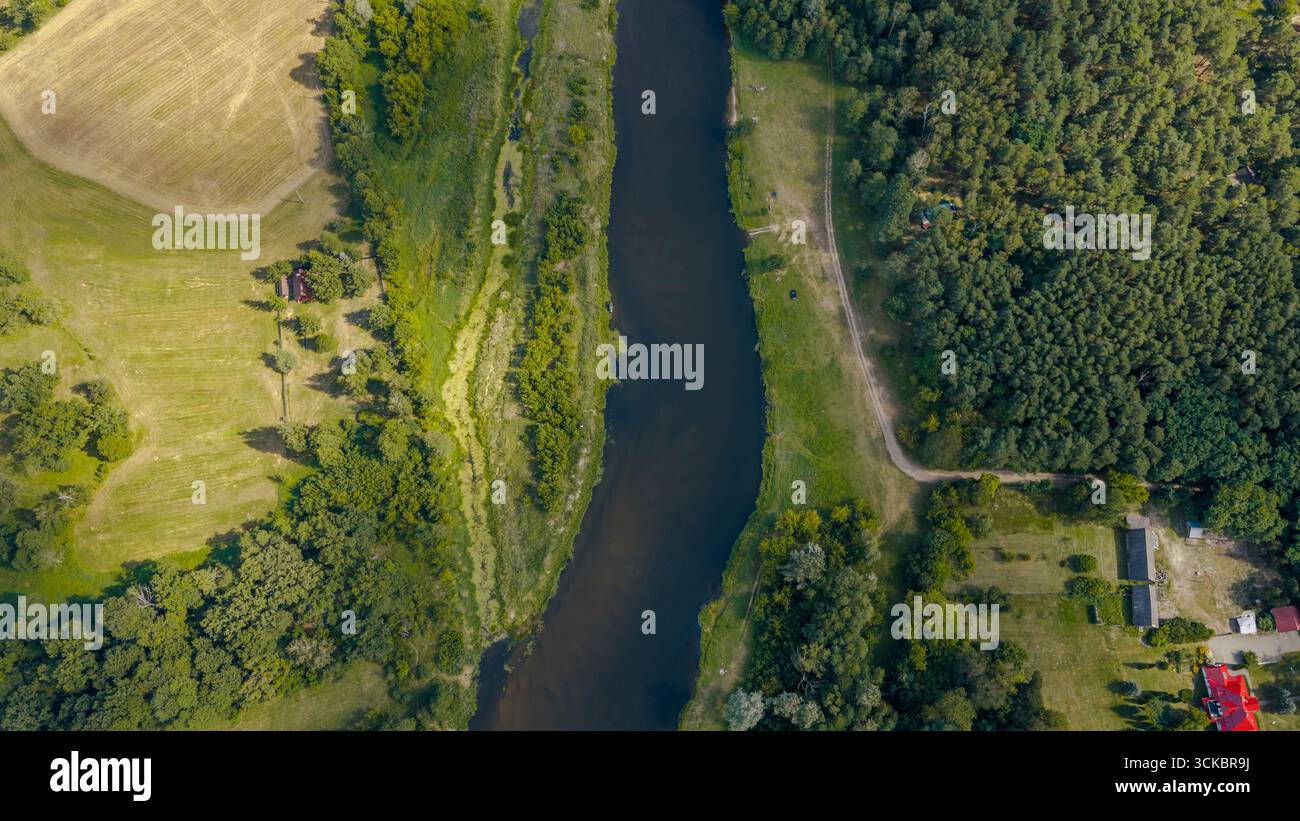Vista aerea di un fiume che si snoda attraverso Nowy Lubiel, Polonia, con campi aperti sulla sinistra, fitta foresta sulla destra e un edificio con tetto rosso visibile Foto Stock