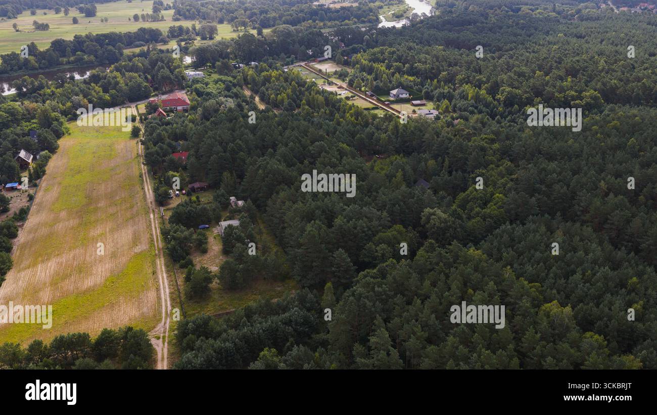Foresta lussureggiante vicino a Nowy Lubiel, Polonia, con una strada sterrata, un fieno, case sparse e un fiume tortuoso in un tranquillo paesaggio rurale. Foto Stock