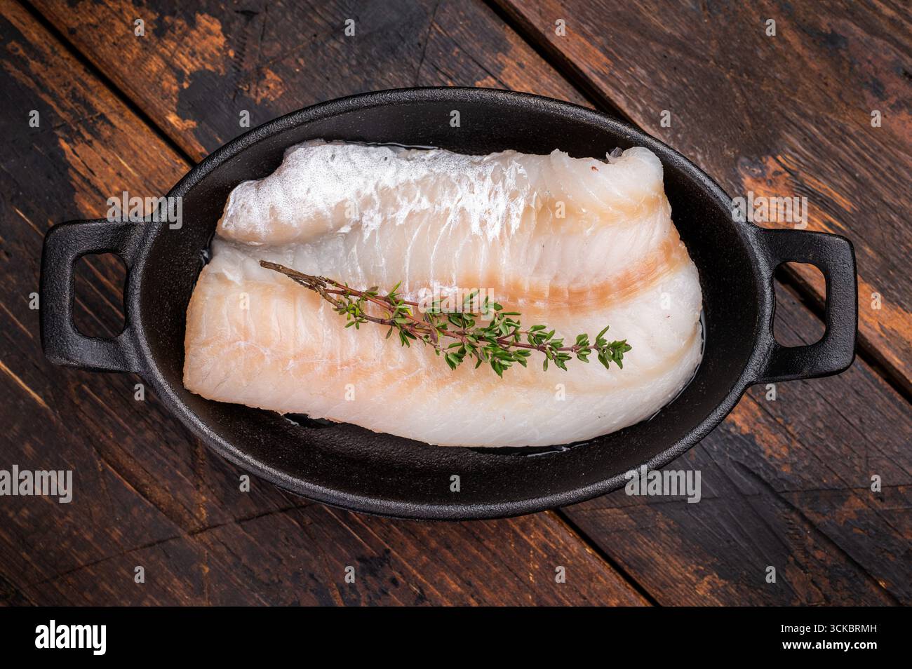 Filetto di merluzzo crudo incontaminato, in attesa di essere marinato e cucinato alla perfezione per una deliziosa esperienza culinaria. sfondo in legno. vista dall'alto. Foto Stock