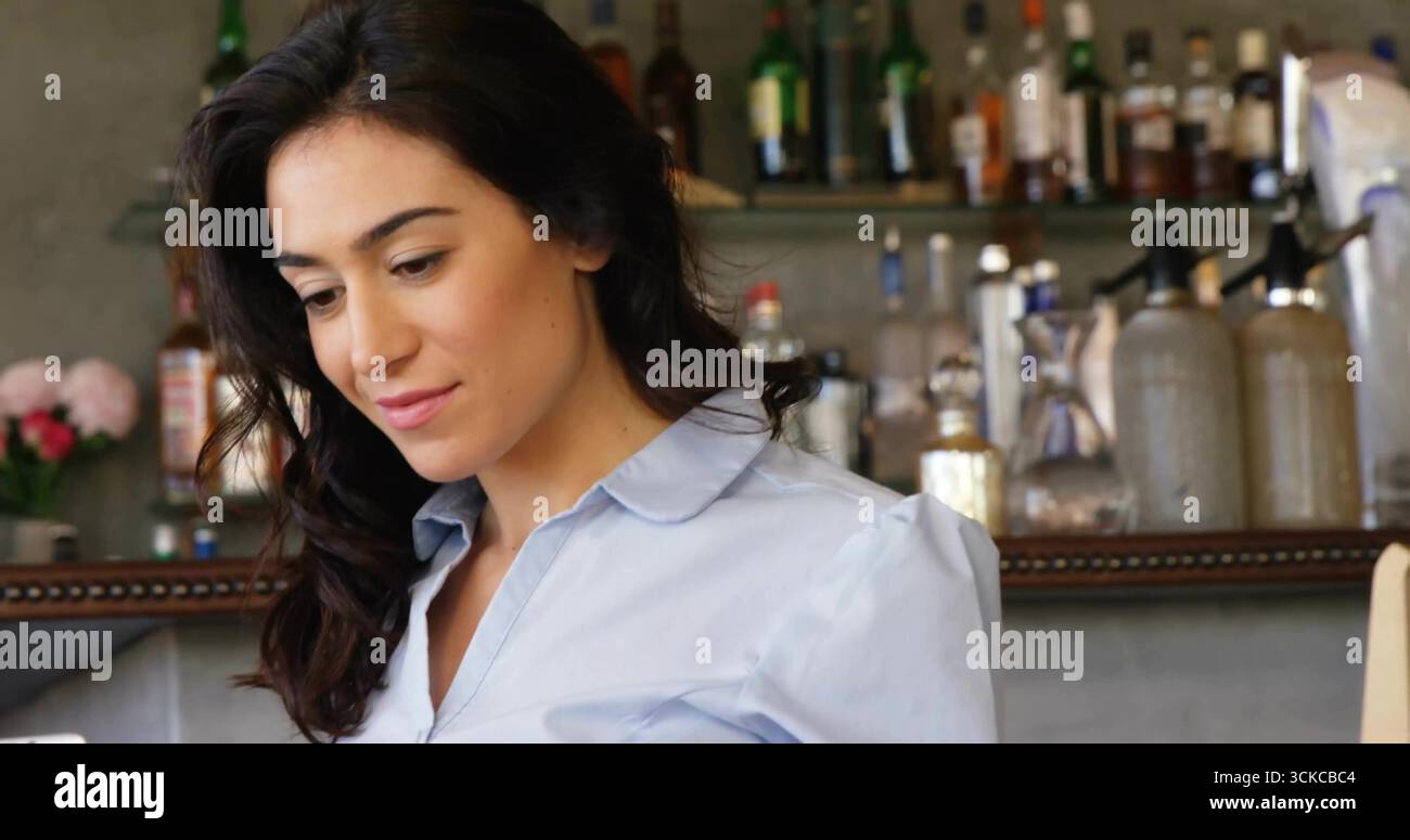 Guardando verso il basso il barista in piedi dietro il banco di legno nel caffè, con peonie rosa, spazio per copiare. Rustico, elegante, professionale, senza tempo, caldo, invito Foto Stock