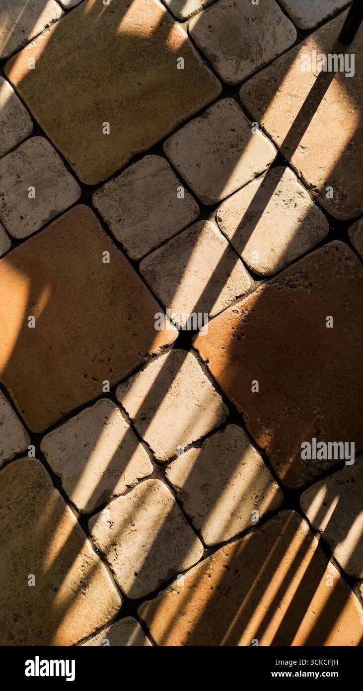 Ombre diagonali alla luce del sole che cadono su un pavimento in pietra con piastrelle quadrate. Geometria urbana astratta, toni caldi, motivi naturali e textur Foto Stock