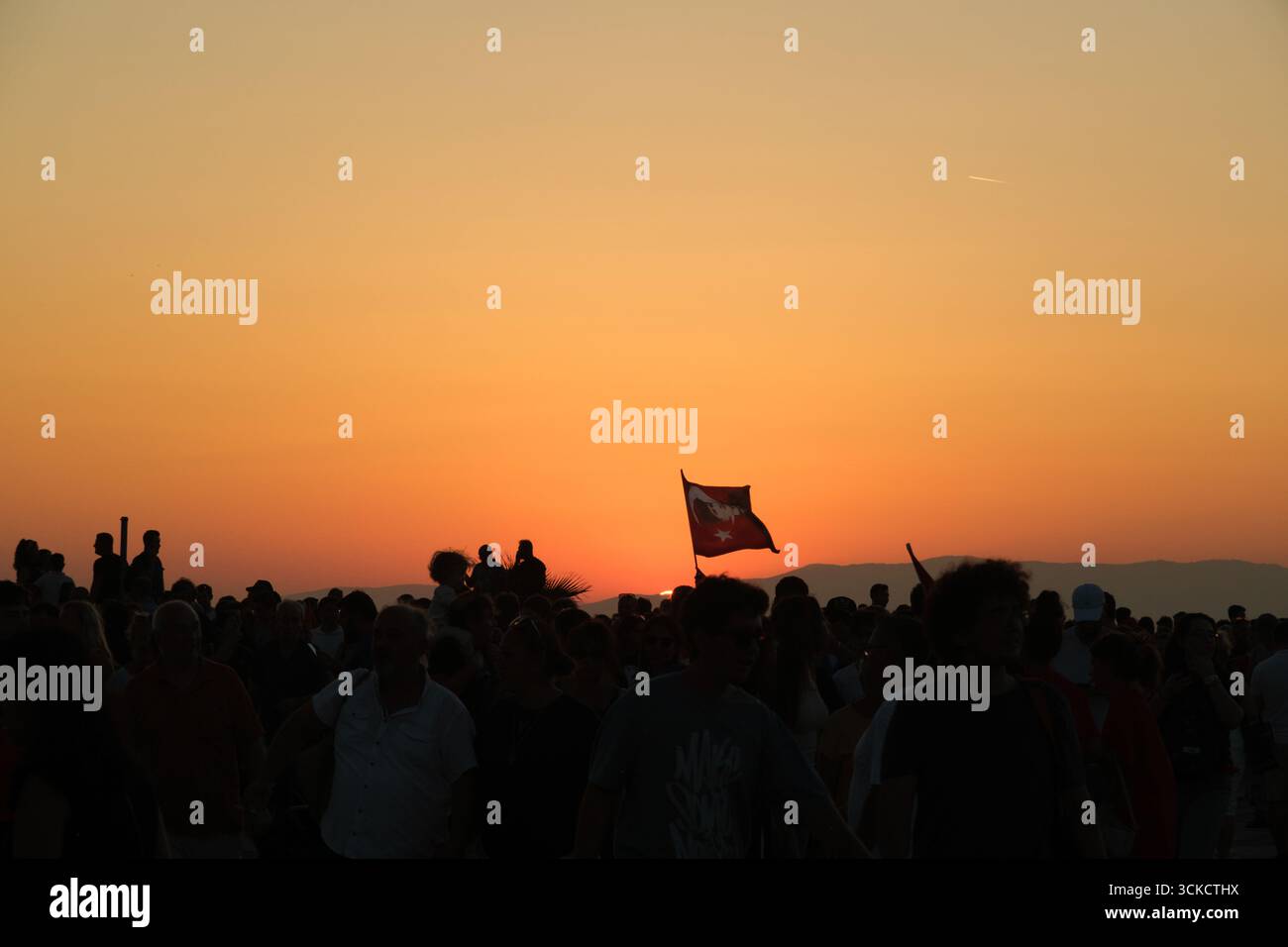 Smirne, Turchia - 9 settembre 2025: Foto di sventolare bandiere turche nel cielo con una folla sagomata al tramonto, scattata durante l'anniversario della liberazione di Smirne Foto Stock