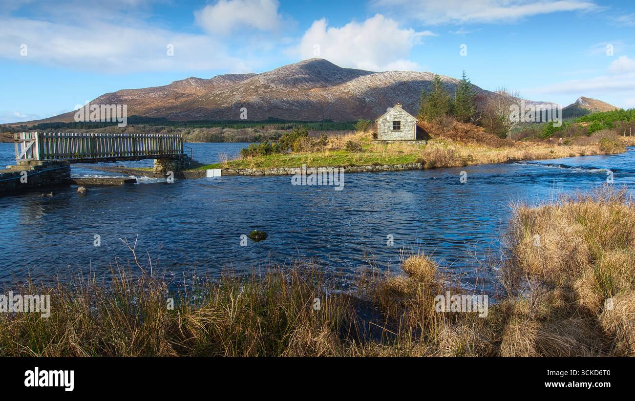 Casa nella natura selvaggia vicino al fiume con montagne nella riserva naturale di At Derryclare nel parco nazionale del Connemara, contea di Galway, paesaggio irlandese Foto Stock