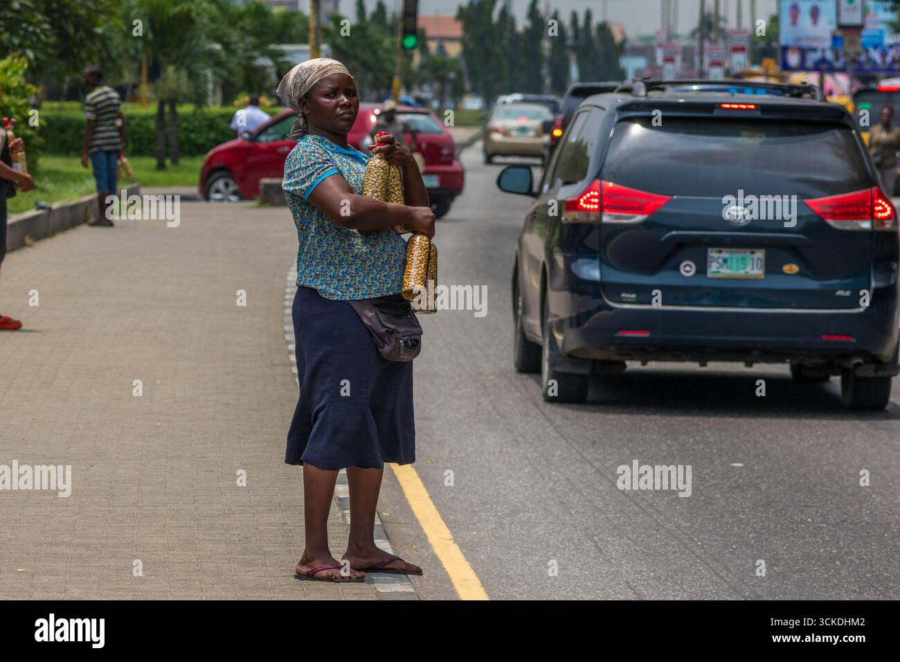 Venditore ambulante che vende arachidi arrostite in bottiglia su una strada affollata a Lagos, Nigeria: Vita urbana quotidiana e cultura locale degli snack nell'Africa occidentale Foto Stock