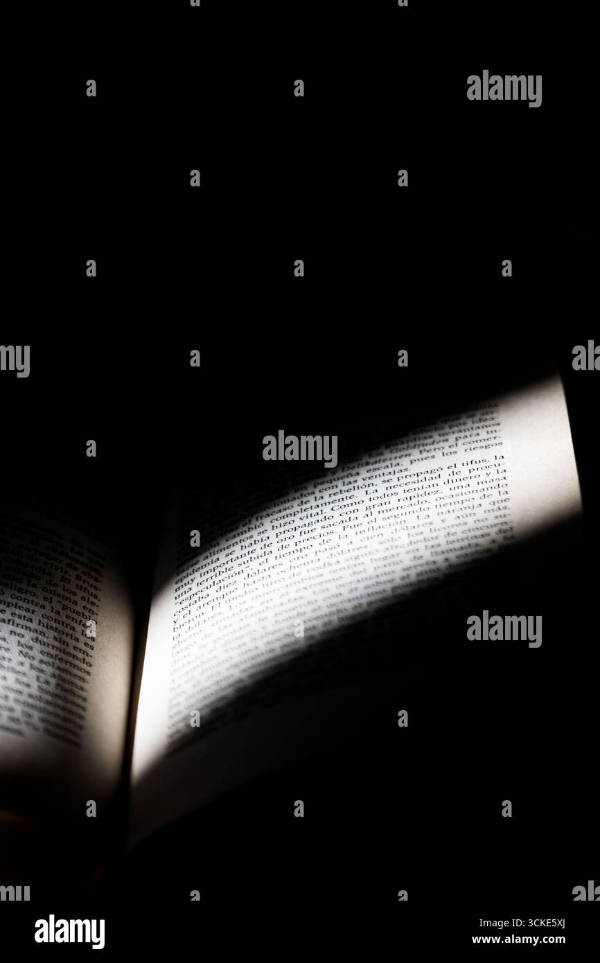 Una pagina di libri attraversata dalla luce in un'atmosfera buia e intima. Foto Stock