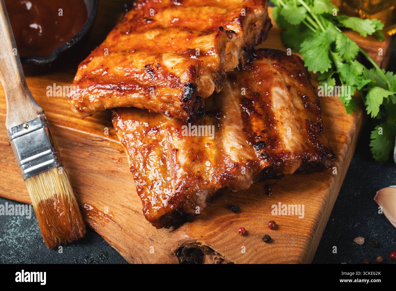 Costolette di ricambio piccanti e grigliate di un barbecue estivo servite con peperoncino caldo e pomodori freschi su un vecchio tagliere in legno vintage Foto Stock