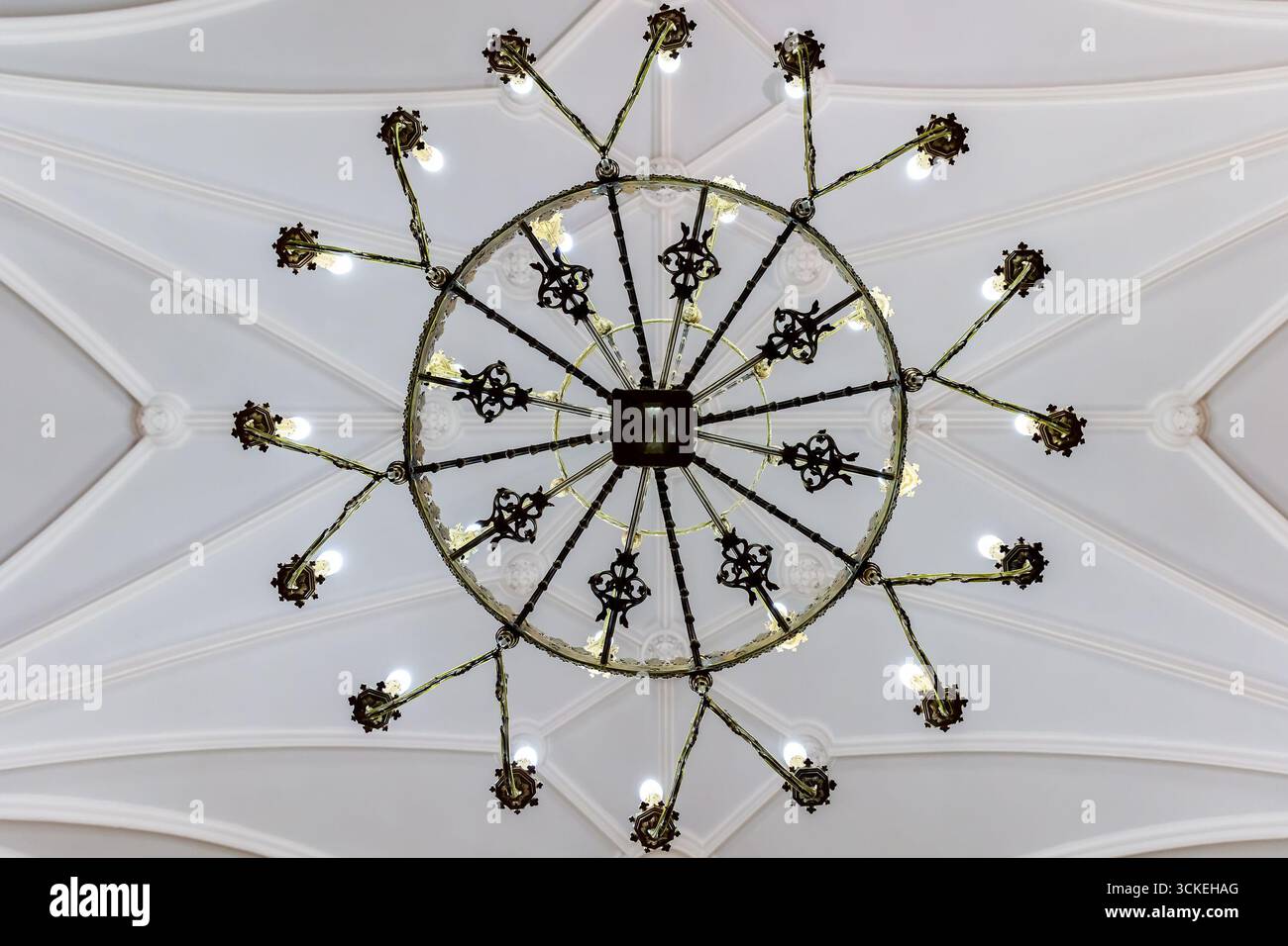 Lampadario circolare simmetrico catturato direttamente dal basso, formando un motivo stellare contro volte gotiche pallide. Composizione architettonica grafica Foto Stock