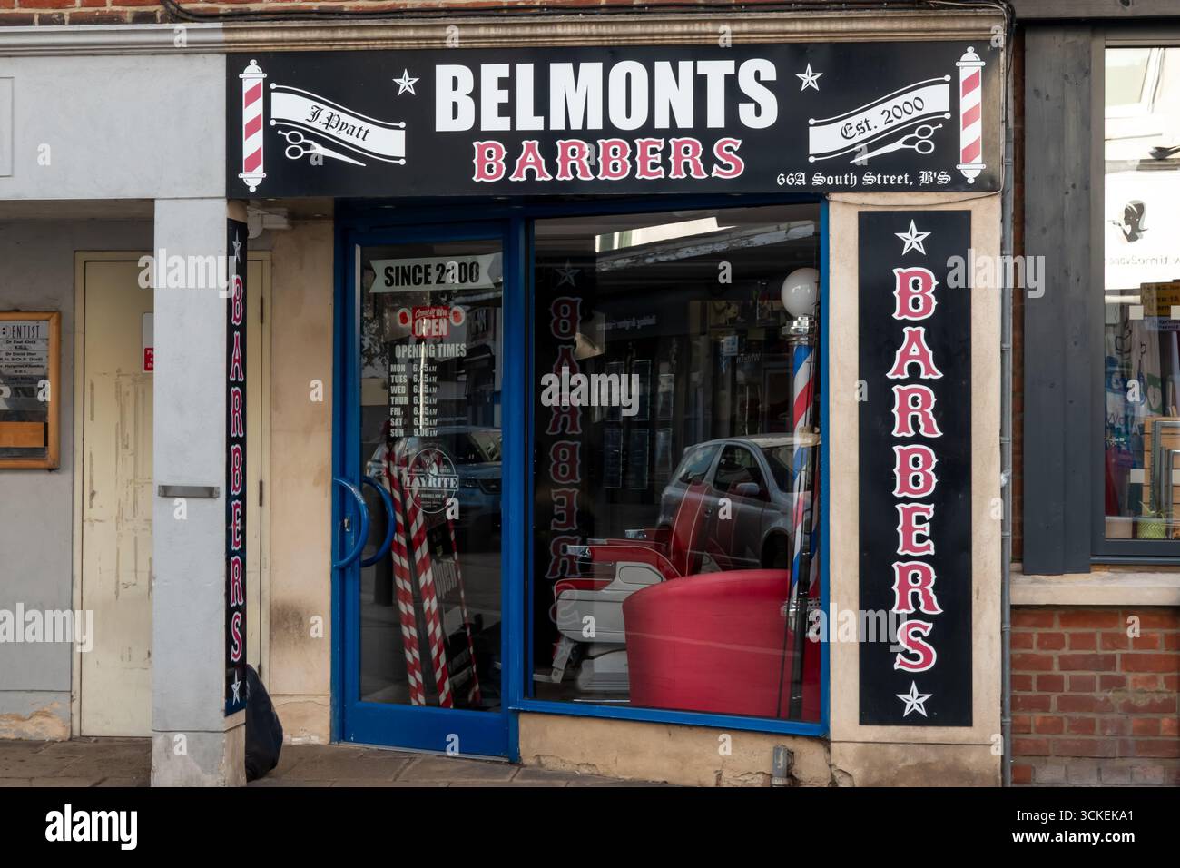 L'esterno di Belmonts Barbers a Bishops Stortford, Hertfordshire, con un tradizionale palo da barbiere e un cartello con il negozio. Foto Stock
