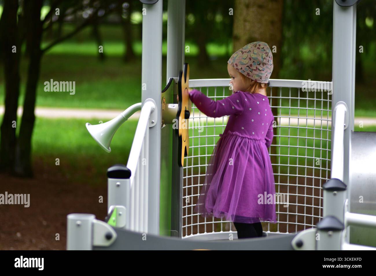Simpatica bambina in abito viola sorridente e giocante con il volante giallo al parco giochi. I bambini si divertono all'aria aperta e amano l'immaginazione durante Foto Stock