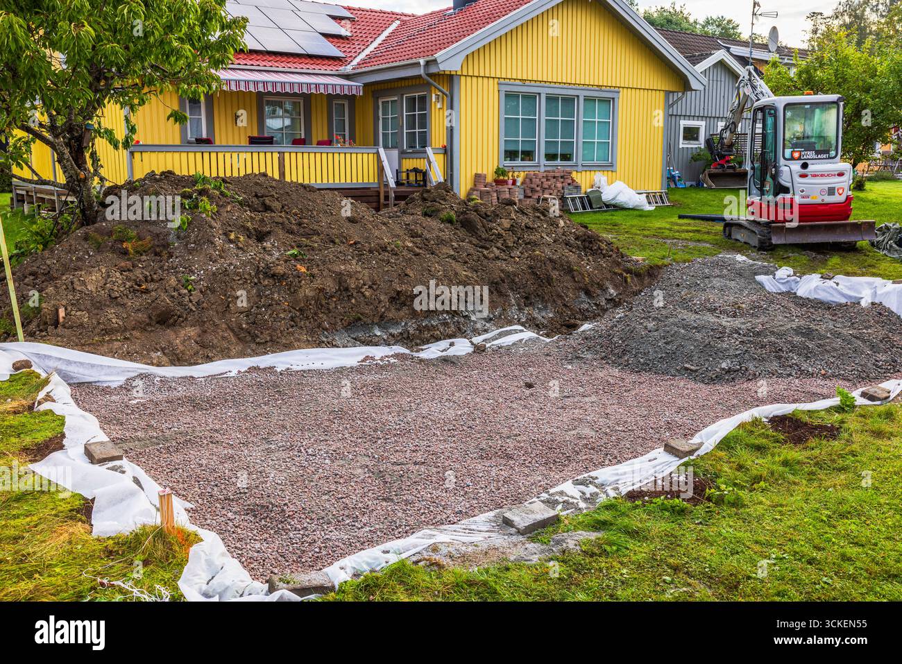 Mini escavatore Takeuchi TB225 in piedi vicino a una casa di legno gialla con pannelli solari durante i lavori di costruzione del cantiere. Svezia. Stoccolma. Foto Stock