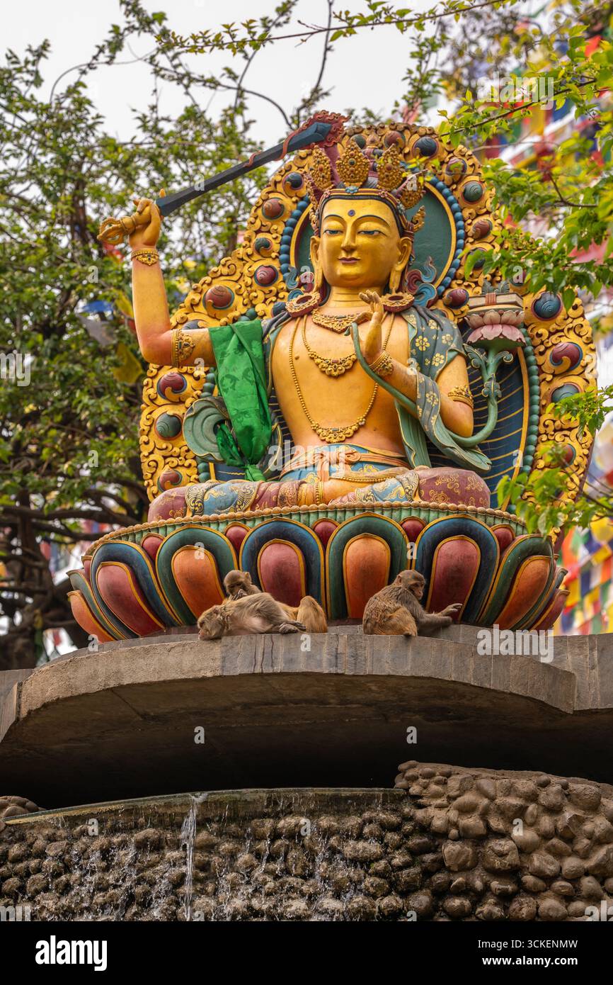 Vibrante statua buddista circondata da elementi naturali con scimmie che riposano alla base di Kathmandu, Nepal. Foto Stock