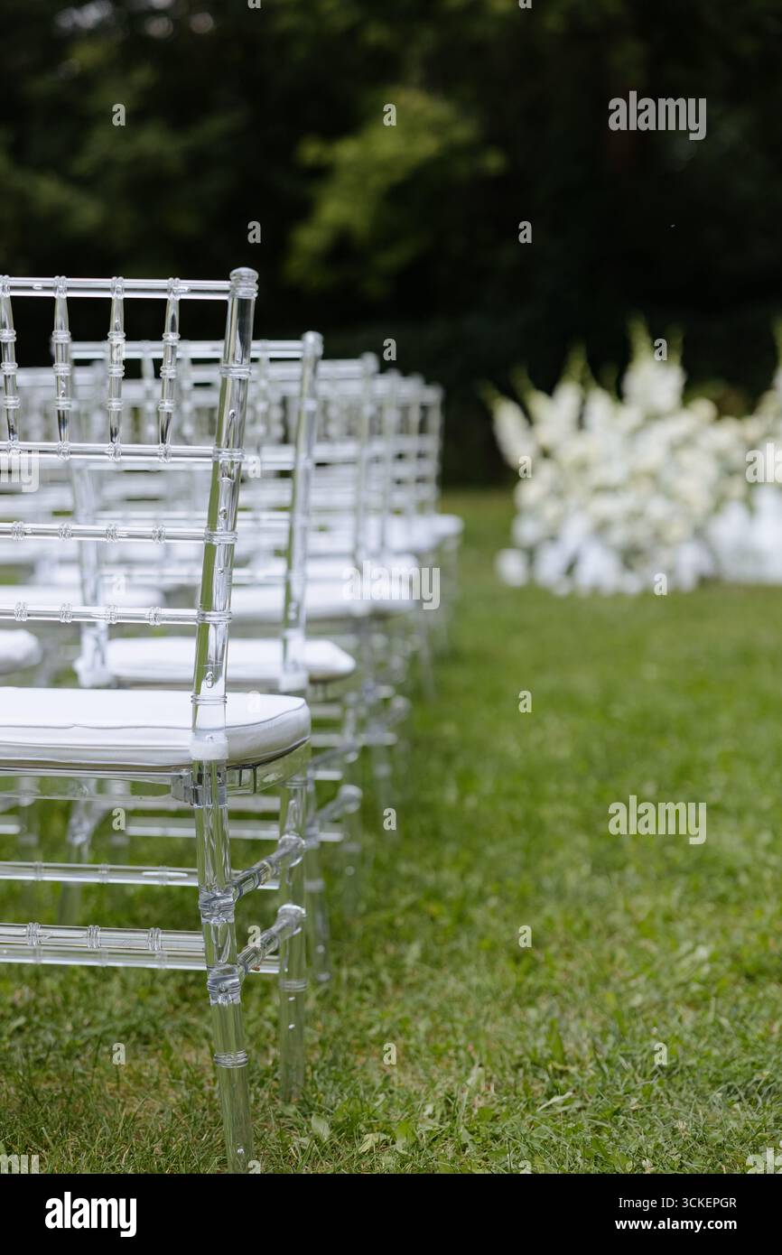 Una squisita disposizione di sedie chiare si trova su un vivace prato, preparandosi per una romantica cerimonia nuziale immersa nella natura. Foto Stock