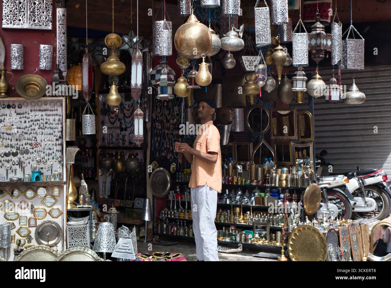 Scena di strada con un venditore in un bazar marocchino - Un affollato mercato con una varietà di lampade tradizionali e artigianato in metallo, con un uomo in piedi in fro Foto Stock