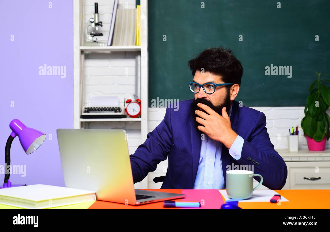 Un insegnante di scuola o un uomo d'affari sorpreso che lavora con un notebook sul posto di lavoro. Apprendimento, istruzione. Studente con occhiali che prende appunti sul notebook. Compiti. St Foto Stock
