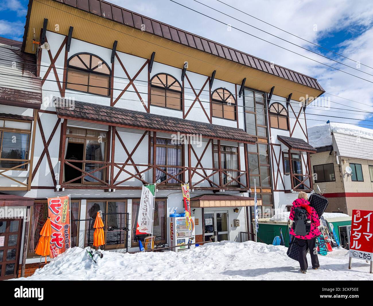 Lo snowboarder che trasporta l'attrezzatura passeggia accanto a un negozio di noleggio presso il resort Ishiuchi, in Giappone Foto Stock