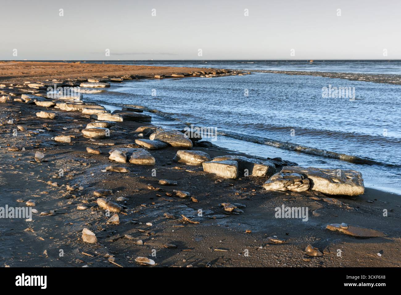 Vista panoramica delle formazioni di ghiaccio che si sciolgono lungo la costa, mostrando dettagli intricati e contrasti contro la sabbia sotto un cielo invernale luminoso. Balt Foto Stock