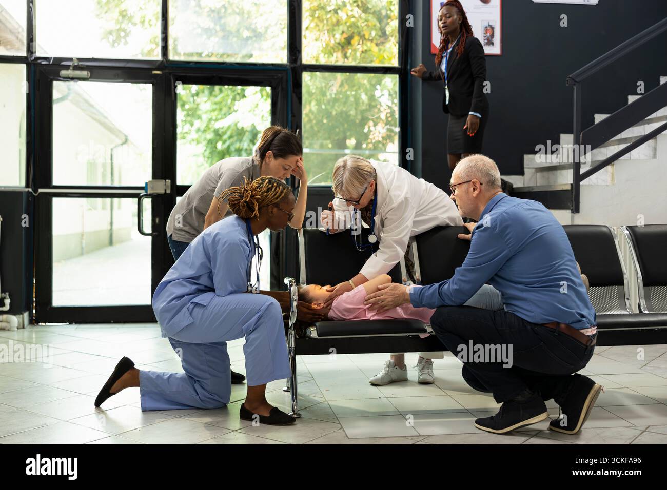 Emergenza familiare nella hall dell'ospedale mentre il bambino perde conoscenza mentre è con la madre, sollecitando un pronto soccorso rapido e il supporto medico da parte di personale esperto addestrato in cure pediatriche urgenti. Foto Stock