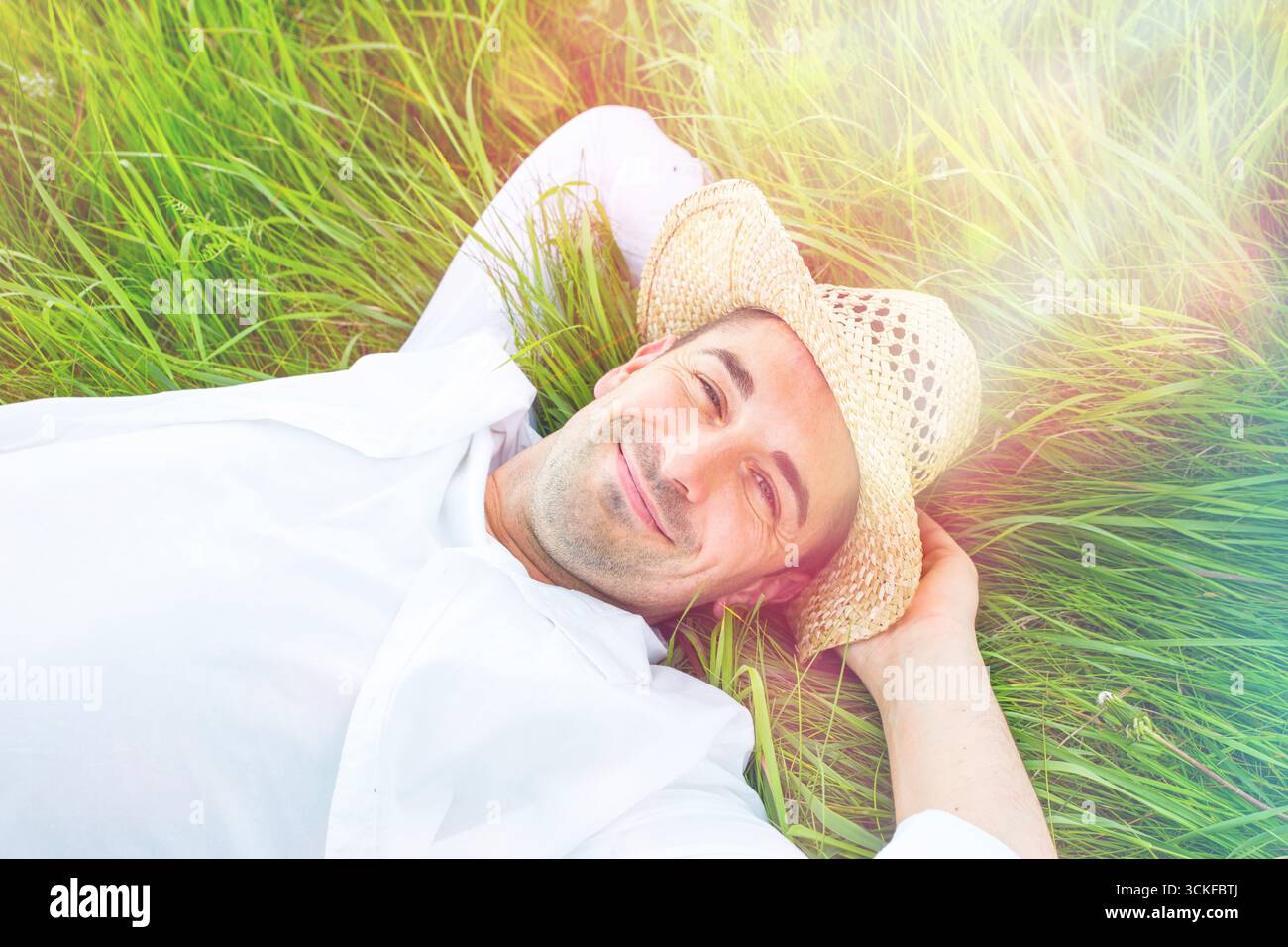 Giovane con cappello di paglia disteso contento su un prato Foto Stock