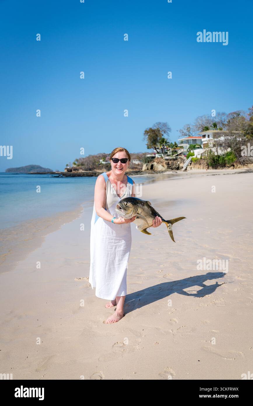 Donna matura felice che mostra pesce appena pescato su una spiaggia di Contadora Island, Panama Foto Stock