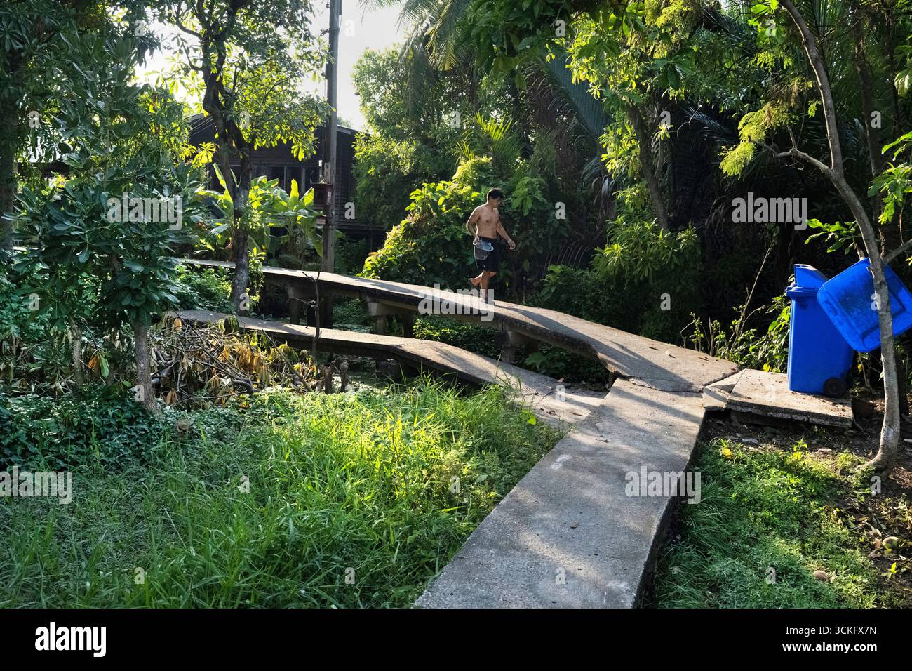 Thailandia - gennaio 26 2025: Gli abitanti locali camminano lungo la passerella, parte di una vasta rete di sentieri, popolari tra i ciclisti, con vegetazione lussureggiante, Waterwa Foto Stock