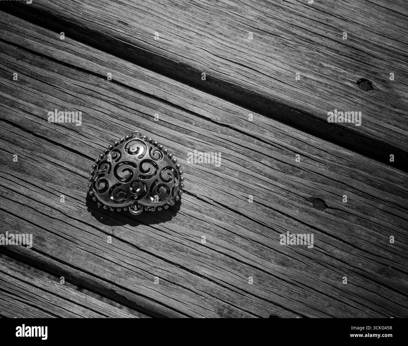 Un ciondolo argentato a forma di cuore poggia su una superficie in legno resistente agli agenti atmosferici. Foto Stock