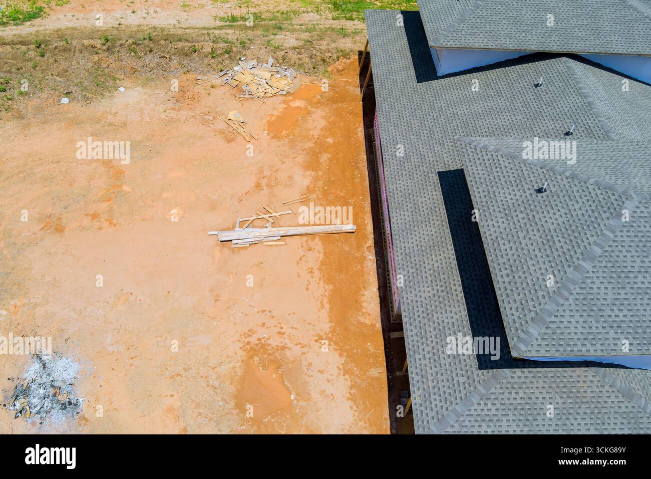 La costruzione di nuove abitazioni presenta nuove tegole rifinite sul tetto di un sito infinito con detriti sparsi nelle vicinanze. Foto Stock