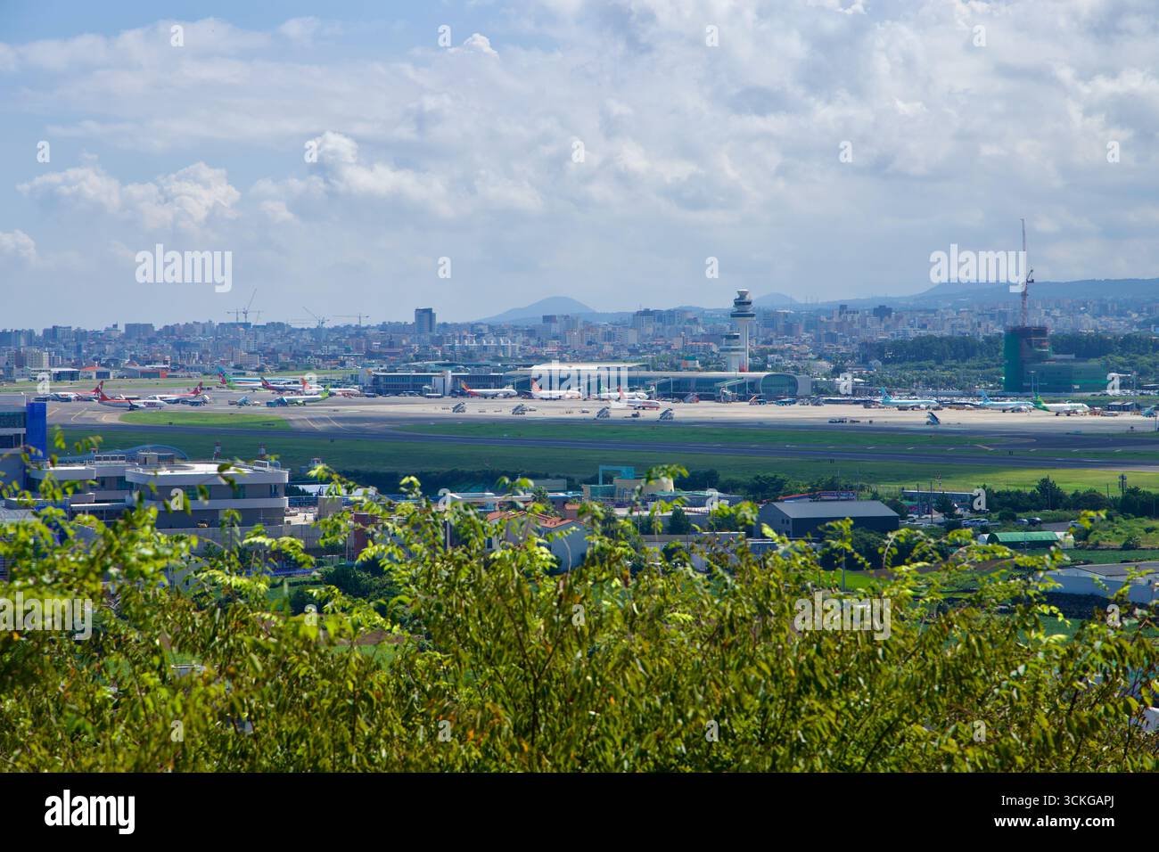Dal punto di osservazione sul Dodu Peak, l'Aeroporto Internazionale di Jeju si estende attraverso la pianura con jet passeggeri, la torre di controllo e il bey dello skyline di Jeju City Foto Stock