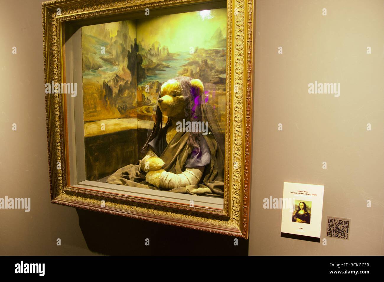 Un orsacchiotto vestito con abiti scuri e velo posa all'interno di una cornice dorata ispirata alla Gioconda di Leonardo da Vinci, con uno sfondo paesaggistico dipinto Foto Stock