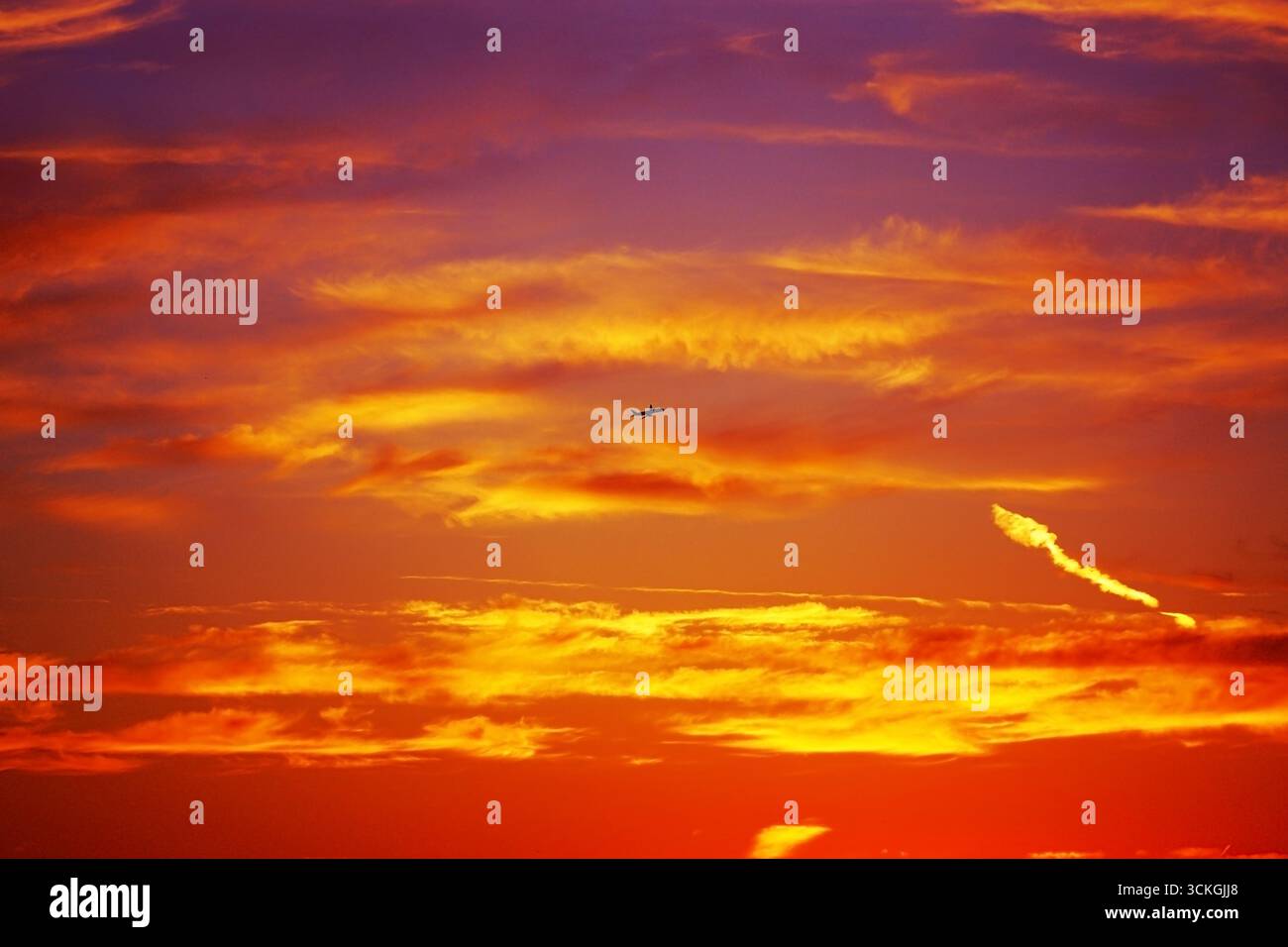 Cielo spettacolare al tramonto con la silhouette dell'aereo che vola attraverso nuvole colorate. I toni ardenti di arancio, giallo e rosso si mescolano creando una vista mozzafiato Foto Stock