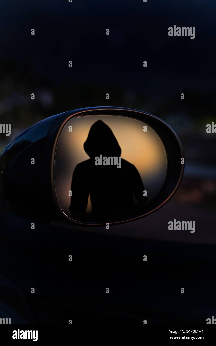 Silhouette con cappuccio riflessa nello specchio laterale dell'auto che simboleggia il crimine informatico, il pericolo o il mistero Foto Stock