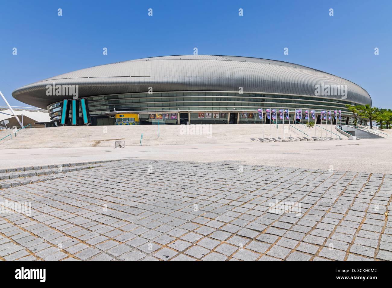 Un'ampia vista al piano terra dell'esterno della MEO Arena, enfatizzando le sue imponenti dimensioni e l'esclusiva forma ellittica con una spaziosa piazza acciottolata Foto Stock