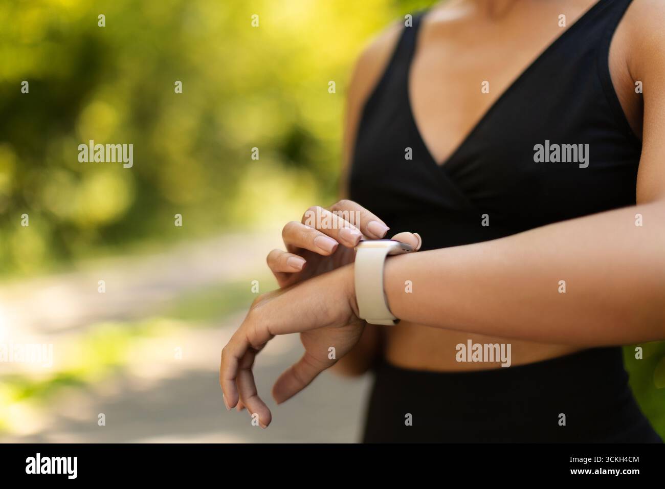 Donna afroamericana irriconoscibile che guarda uno smartwatch durante gli allenamenti all'aperto Foto Stock
