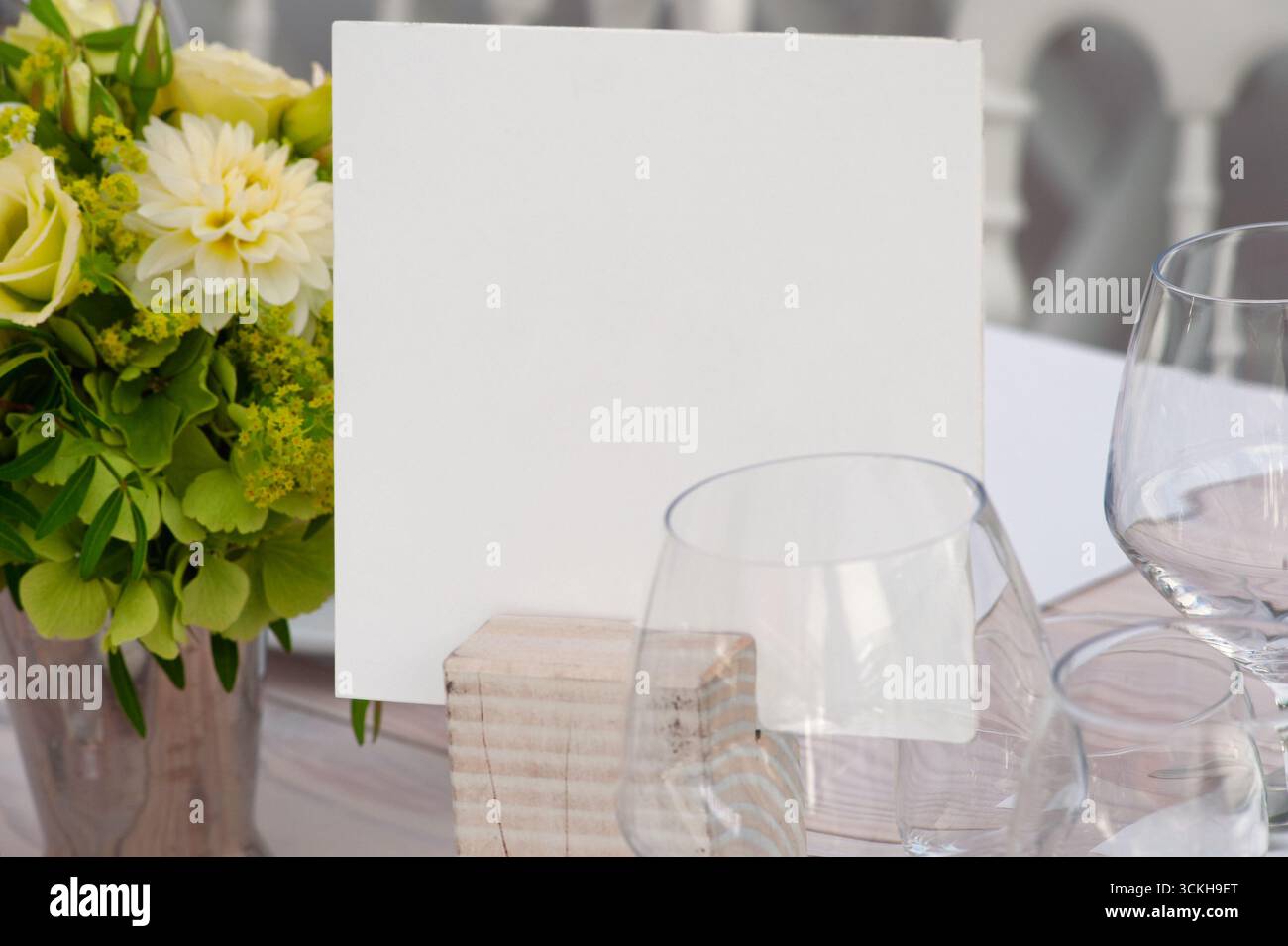 Un tavolo di classe con una carta bianca su un supporto in legno, completato da fiori vivaci e bicchieri da vino, perfetto per matrimoni, banchetti e Foto Stock
