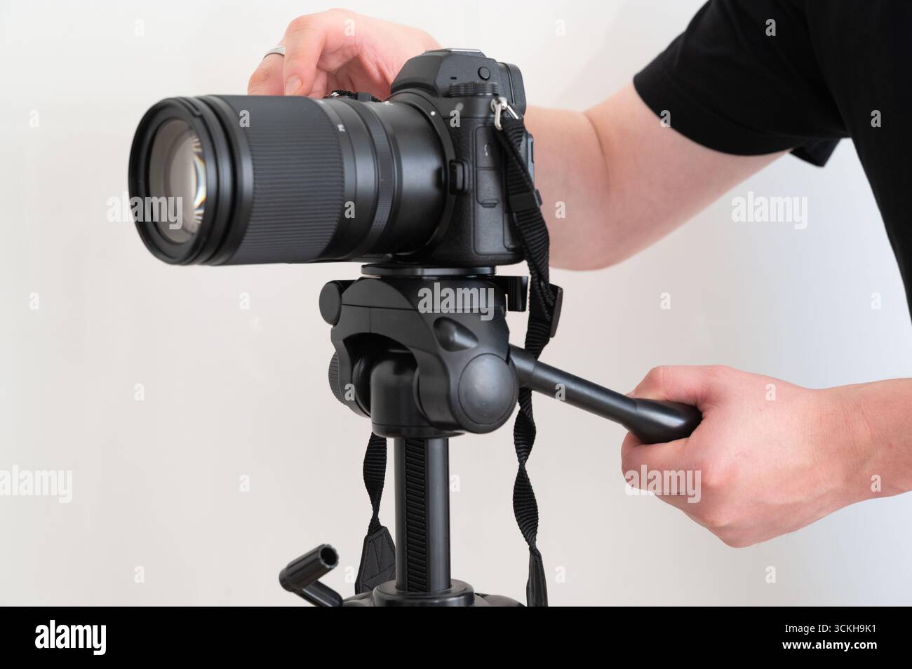 Un fotografo esperto regola attentamente le impostazioni di una fotocamera DSLR posizionata su un robusto treppiede Foto Stock