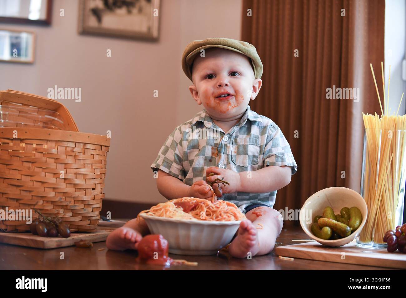 Sorridente con il viso disordinato che gioca con uva e spaghetti. Foto Stock