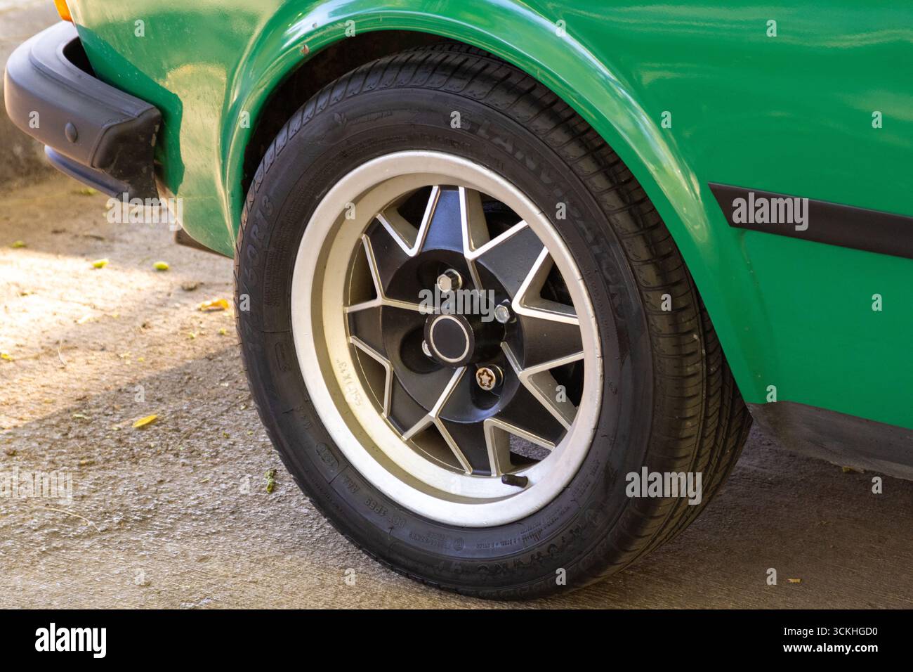Cerchi in lega lucida con dettagli neri su una classica auto verde parcheggiata su una superficie in cemento, che mostra un design automobilistico vintage Foto Stock