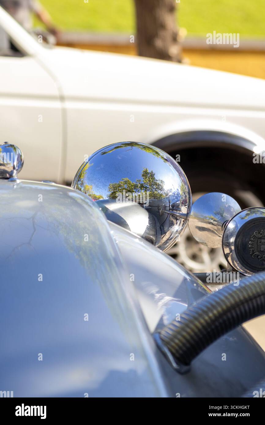 I fari cromati brillanti riflettono le auto e gli alberi parcheggiati su un veicolo d'epoca, mostrando la storia e il design dell'auto Foto Stock