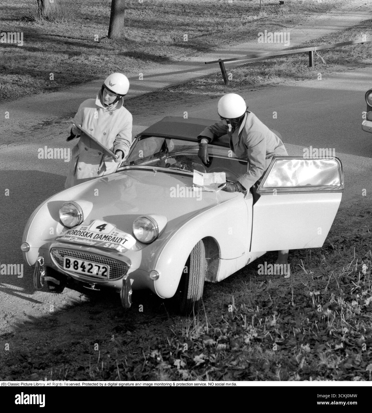 Austin-Healey Sprite MK1 Frogeye: Icona del Rally Spirit degli anni '1960. In questa vibrante immagine del 1960 del Nordic Women's Rally, due partecipanti femminili si trovano accanto alla Austin-Healey Sprite MK1 "Frogeye", un'auto sportiva britannica compatta celebrata per i suoi fari sgargianti e simili a rane e per il rivoluzionario design monoscocca. Lanciata nel 1958 da Donald Healey Motor Company sotto la guida di BMC, la Sprite offriva un divertimento accessibile con un motore da 948 cc serie A da 43 cv, trazione posteriore e un telaio leggero da 1.500 lb, ideale per una guida vivace e per gli sport motoristici. Il suo significato risiede nella democratizzazione dello sport CA Foto Stock