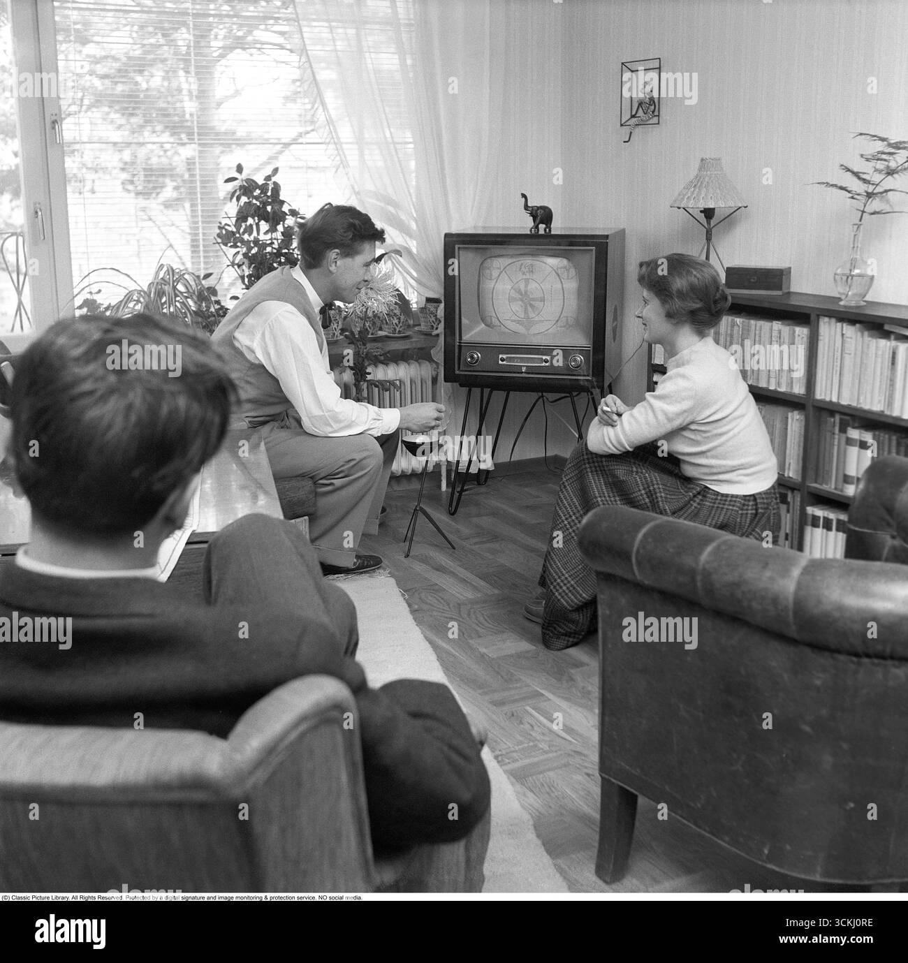 Televisione negli anni '1950 Un design tv tipico dell'era, con la possibilità di visualizzare solo trasmissioni in bianco e nero e un solo canale. Le manopole sui comandi anteriori consentono di controllare l'immagine e l'audio. Le trasmissioni televisive in Svezia sono iniziate ufficialmente il 15 settembre 1956, lanciate da Radiotjänst con il programma Sigge slår på stora trumman. È il personaggio televisivo Pekka Langer con la sua famiglia a casa nel 1957. Sullo schermo, è visibile il modello di test classico. Durante gli anni '1950, la televisione era un mezzo nuovo e in rapida evoluzione. I set erano ingombranti, spesso alloggiati in armadi di legno, e presentavano un piccolo stativo Foto Stock