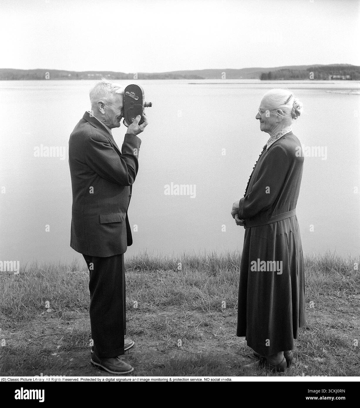 La sta filmando. Una coppia anziana, dove la cattura in un film con una telecamera Keystone A-7 degli anni '1930 Si tratta di una telecamera da 16 mm, caricata manualmente con film che sono stati successivamente sviluppati e proiettati su uno schermo di proiezione a casa. La Keystone A-7 era una popolare fotocamera amatoriale del suo tempo: Compatta, robusta e a manovella. 1950 Svahn Foto Stock