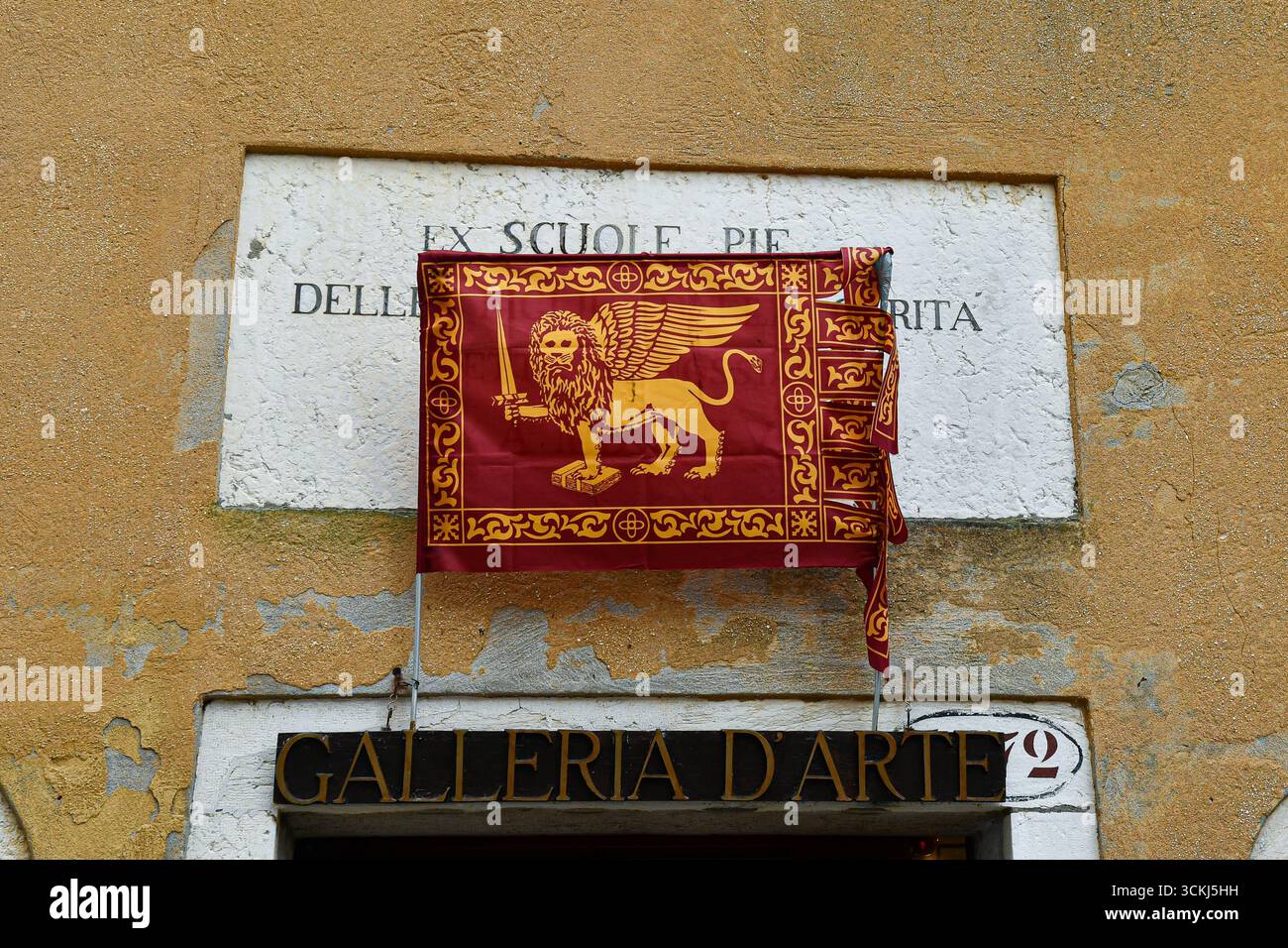 La bandiera veneziana copre parzialmente il vecchio segno delle "ex scuole delle Figlie della Carità" in un edificio che oggi ospita una galleria d'arte, Venezia, Italia Foto Stock