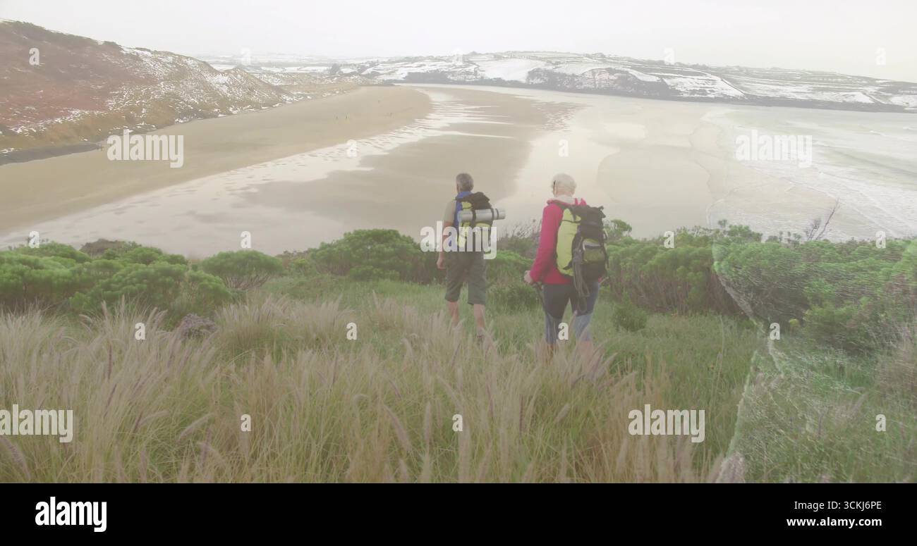 In piedi due escursionisti che osservano pendii erbosi che si affacciano sulla spiaggia sabbiosa, con zaini e stivali Foto Stock